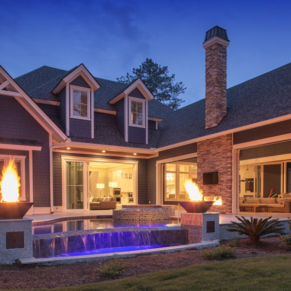 Backyard of home at night with fire features and a pool with waterfall