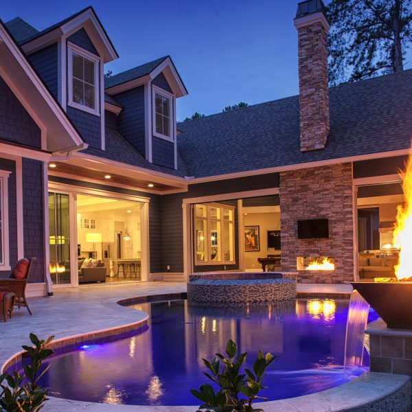 Backyard of home at night with fire feature and a pool with waterfall