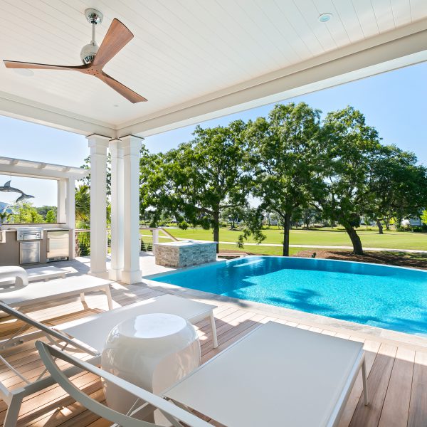 Backyard infinity pool viewed from the home patio with lounge chairs and a grilling station