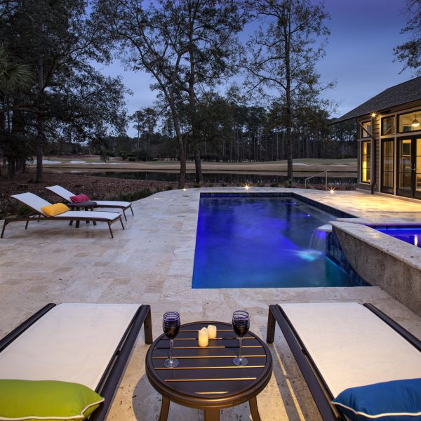 L shaped pool at night with lounge chairs and red wine glasses