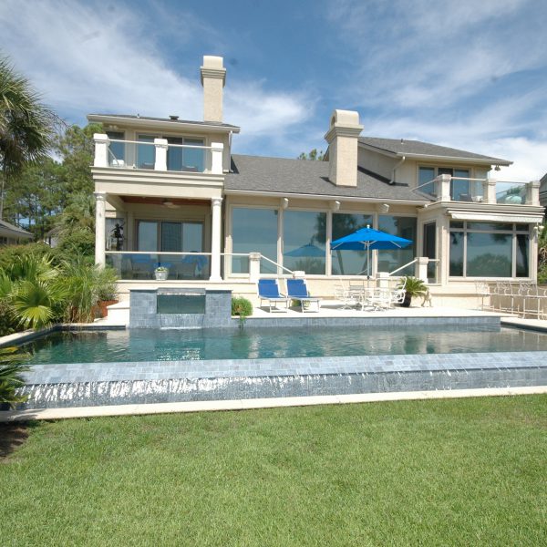 Front view of infinity pool, water fall feature and back of a beach house