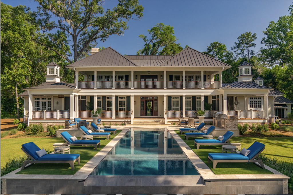Back of large home with pool and multiple blue lounge chairs