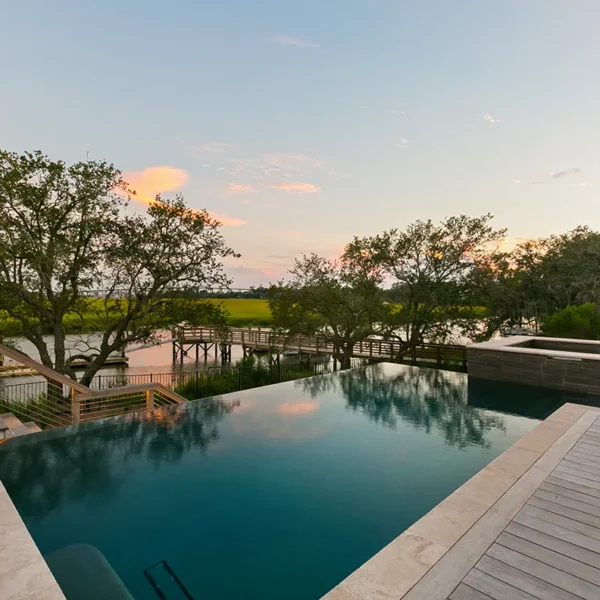 Infinity pool with river marsh view and wooden deck at sunset