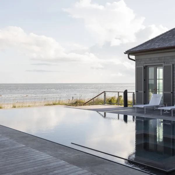 Oceanfront infinity pool with lounge chairs and a modern beach house.