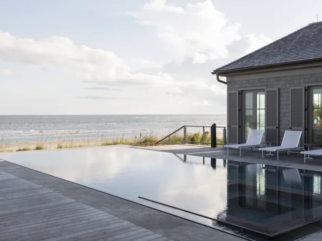 Oceanfront infinity pool with lounge chairs and a modern beach house.