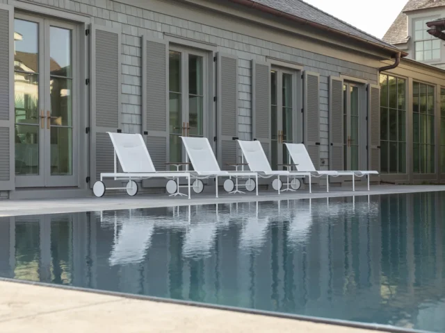 Modern backyard pool with white lounge chairs and a gray house.