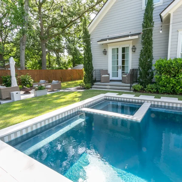 Beautifully landscaped garden pool with integrated spa next to a modern cottage-style home.