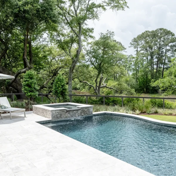 Spa and pool surrounded by expansive patio and lush forest views, featuring stylish poolside loungers.
