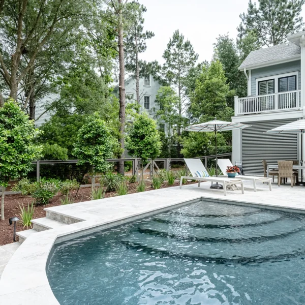 Contemporary home with private poolside seating and large patio umbrellas surrounded by mature trees.