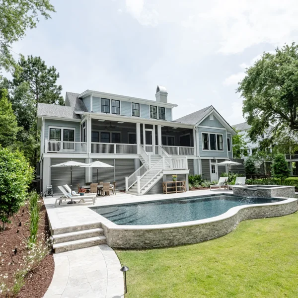 Wide-angle view of a grand backyard with curved pool, hot tub, and a large two-story home with screened porch.
