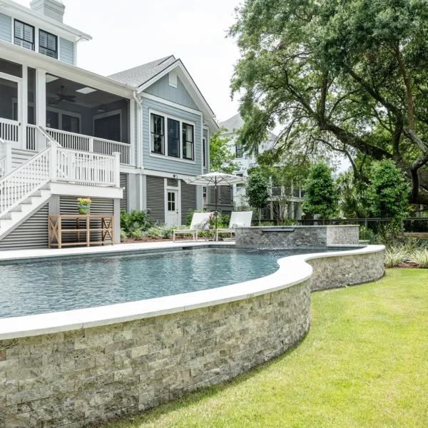 Curved edge pool with stone surround and greenery, adjacent to a modern gray home with white accents.