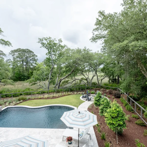 Elevated aerial view of a forest-lined backyard with a curved pool, spa, and fire pit entertaining area.