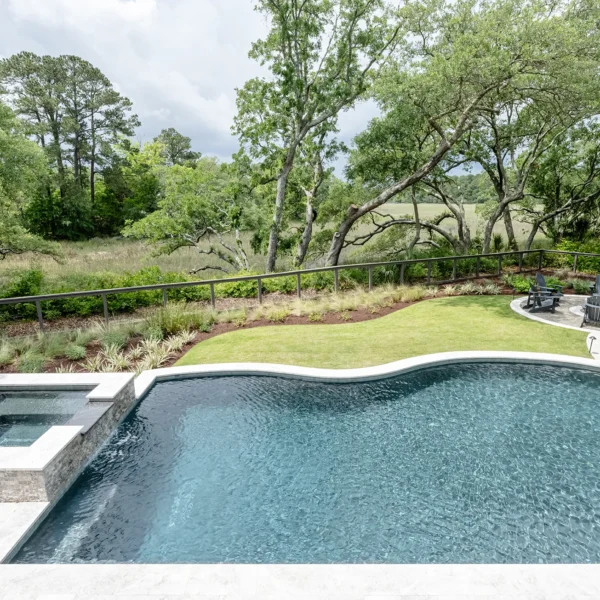 Elevated view of a curved pool with attached hot tub overlooking scenic greenery and a fire pit area.