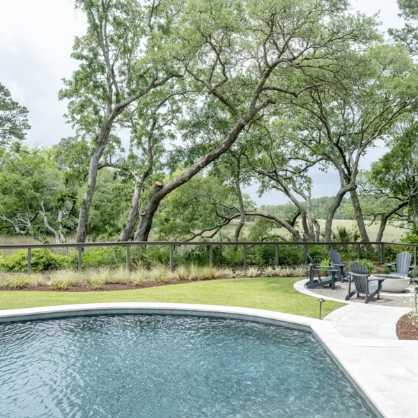 Peaceful backyard fire pit lounge area next to a curved pool surrounded by mature trees and landscaping.