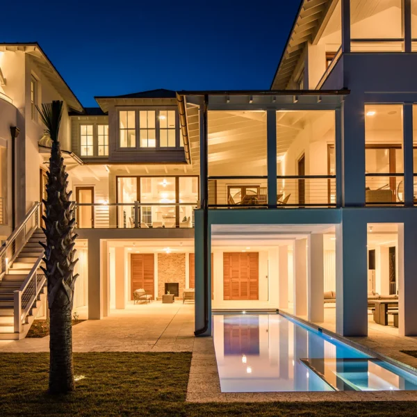 Luxury home exterior at dusk with illuminated pool and outdoor living spaces.