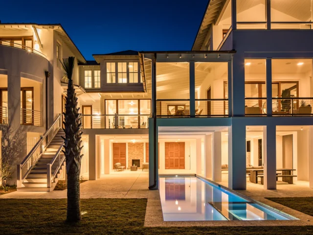 Luxury home exterior at dusk with illuminated pool and outdoor living spaces.