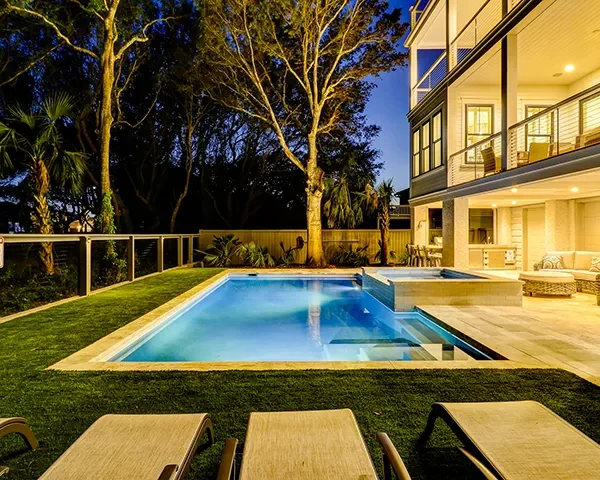 Luxury pool illuminated at night with warm lighting and forest surroundings.