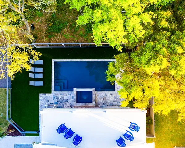 erial view of a luxury backyard pool surrounded by lush greenery and modern lounge chairs.