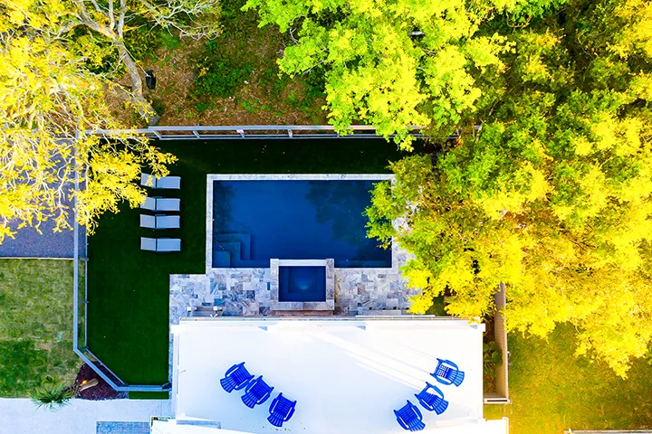 aerial view of a luxury backyard pool surrounded by lush greenery and modern lounge chairs.