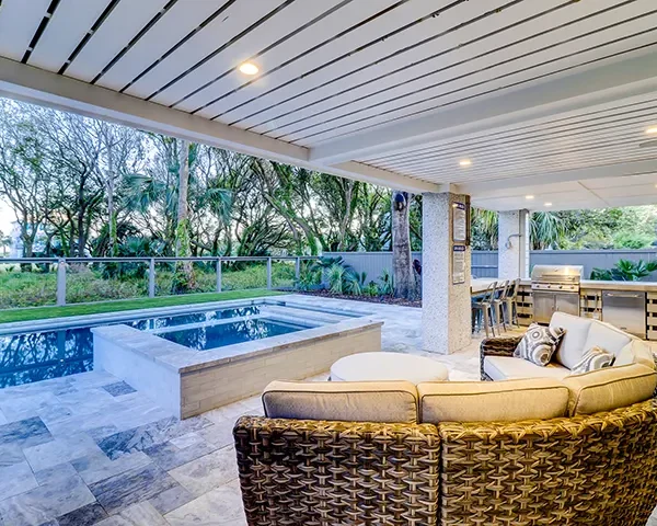 Covered outdoor patio with plush seating and built-in grill overlooking a sleek pool and spa.