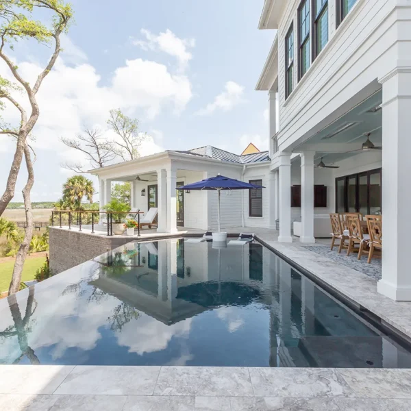 Elegant infinity pool next to covered patio with lounge seating and umbrellas