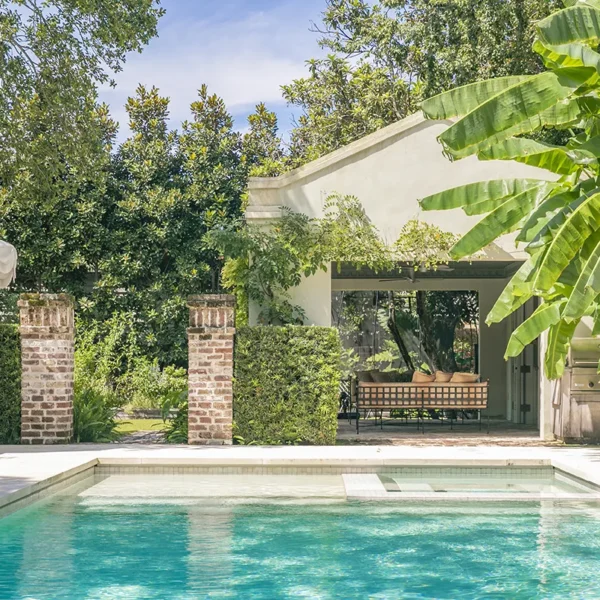 Lush backyard swimming pool with tropical plants and outdoor lounge.