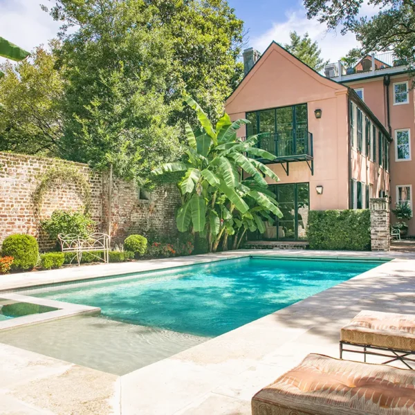 Backyard pool and spa with surrounding greenery and a pink house.