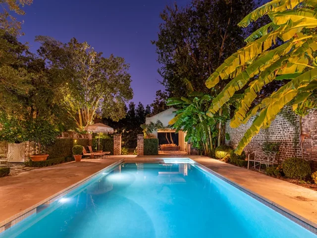 Tranquil backyard pool at night with ambient lighting and tropical foliage.