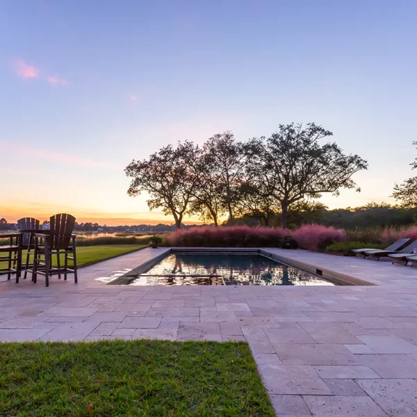 Tranquil sunset view of a backyard pool, patio, and waterfront landscape.