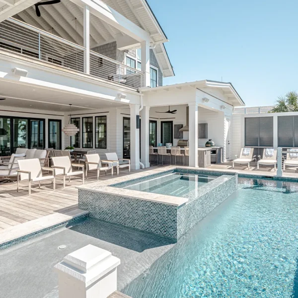Covered outdoor lounge and dining area with an elevated infinity spa and ocean-facing pool at a coastal home