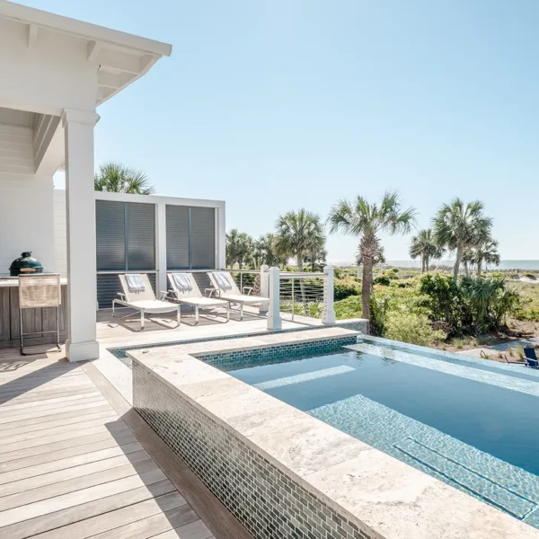 Oceanfront pool deck with sun loungers, outdoor grill area, and view of beach path