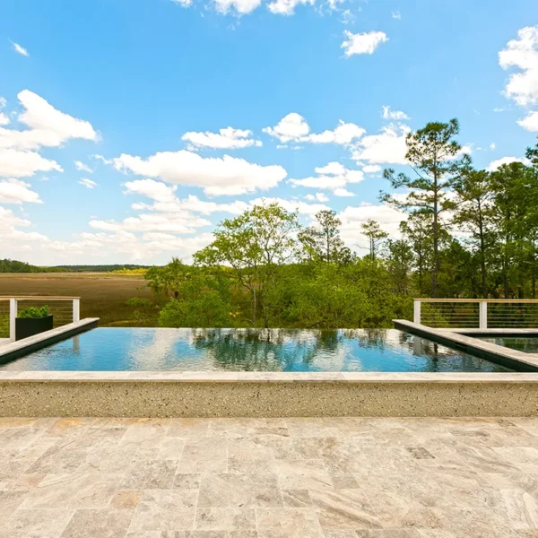 Symmetrical view of a raised infinity-edge pool and spa framed by trees and blue sky with clouds.