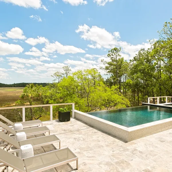 Angled perspective of elevated pool and spa with marshland views and sleek lounge seating."