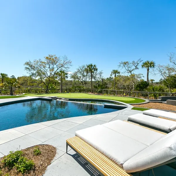 Contemporary pool with white cushioned loungers and a lush backdrop of palm trees and landscaping.