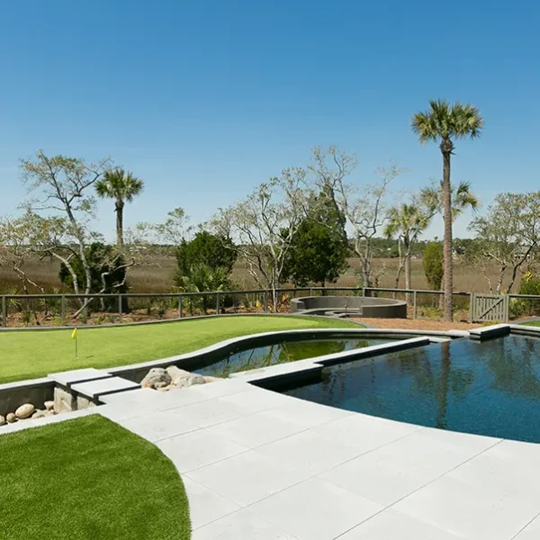 Seamless integration of putting green and luxury pool bordered by palm trees and a sleek stone patio.