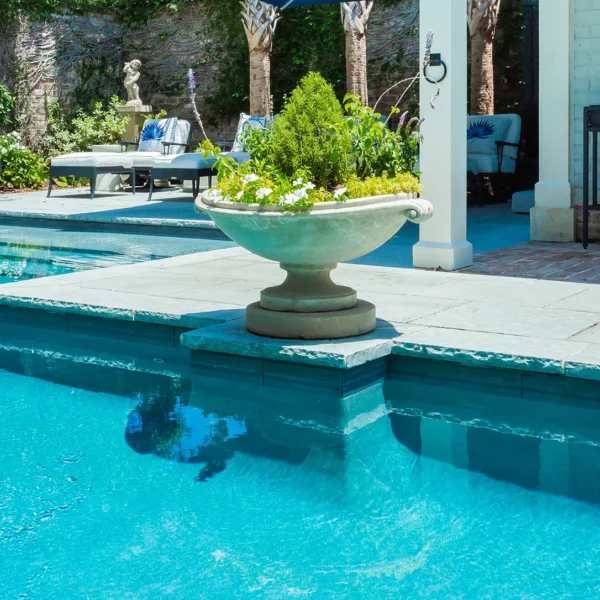 Close-up of a backyard pool with a decorative planter and lounge furniture.