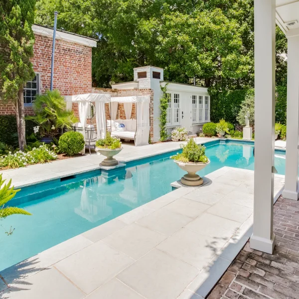 Rectangular swimming pool in a lush backyard with patio and lounge chairs.