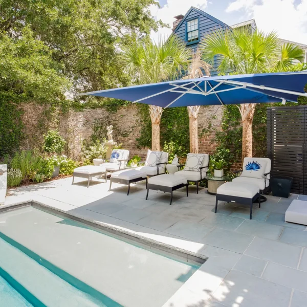 Modern backyard pool with lounge chairs under a large blue patio umbrella.
