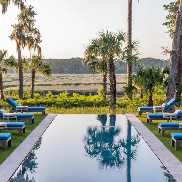 Long rectangular pool with blue chaise lounges set against marsh and tree-lined backdrop