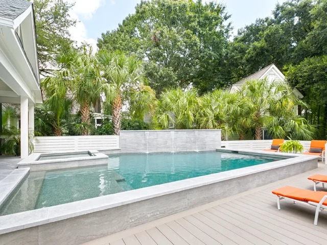 Modern pool with spa, waterfall, and palm tree landscaping.