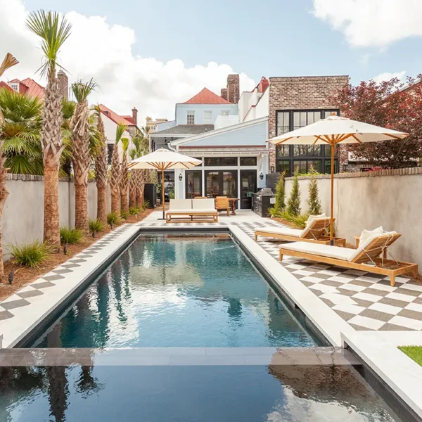Long, narrow backyard pool with checkered patio, lounge chairs, and umbrellas.