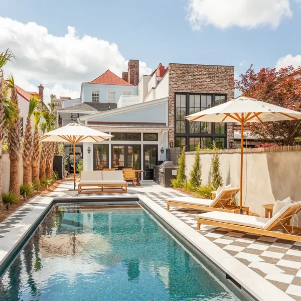 Backyard swimming pool with lounge chairs, umbrellas, and surrounding urban landscape.