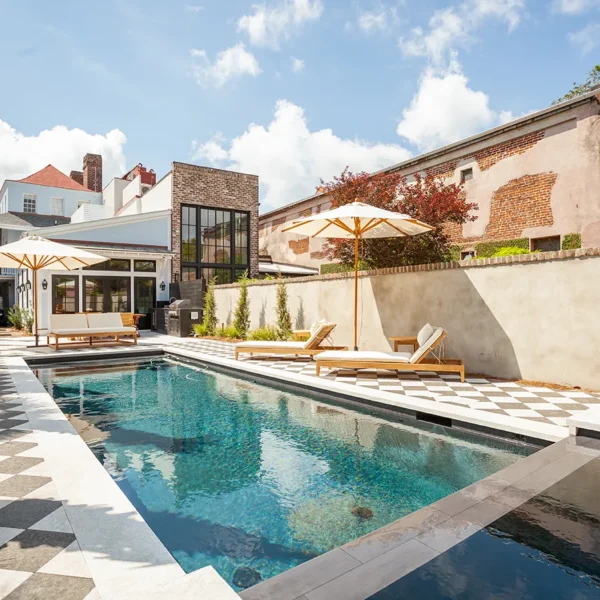 Backyard swimming pool with a checkered patio, lounge furniture, and surrounding buildings.