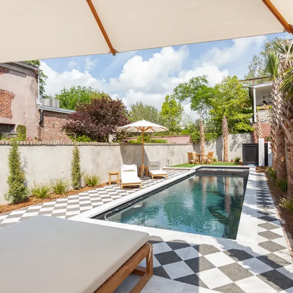 Backyard pool with a checkered patio, lounge chairs, and palm trees under a patio umbrella.