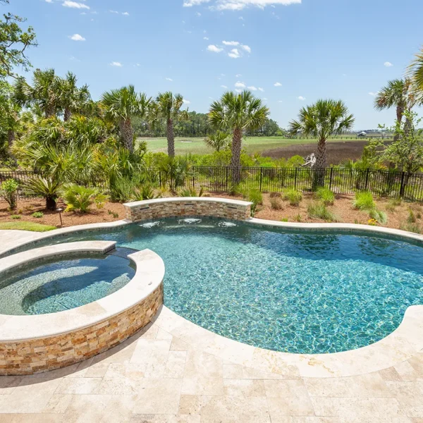 Freeform swimming pool with attached spa and lush tropical surroundings.